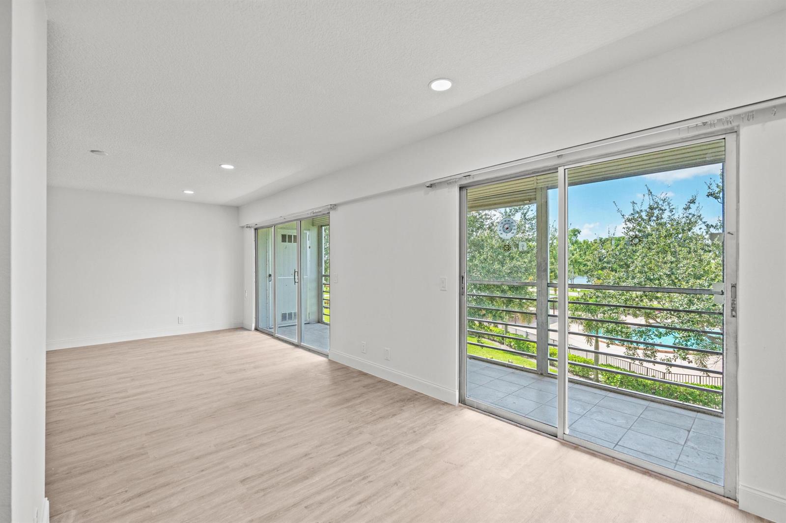 An empty room with light wood-look flooring, recessed lighting, and sliding glass doors to a balcony — 204 Mansfield E # 204, Boca Raton FL 33434, BOCA RATON, FL