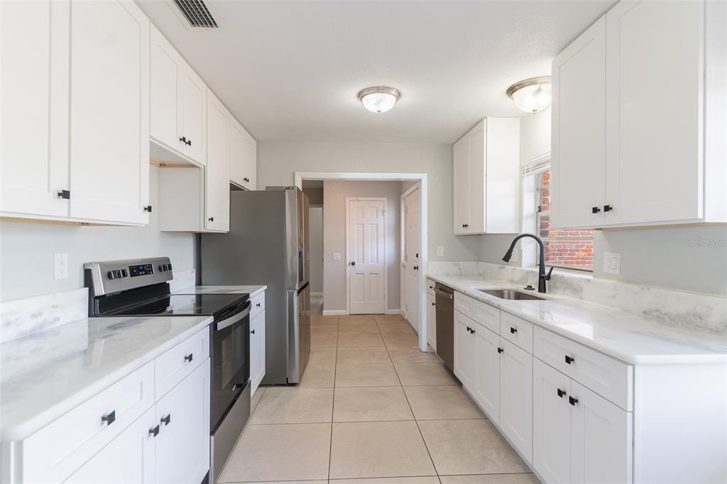 A kitchen features white cabinetry, stainless steel appliances, marble countertops, and light tile flooring — 124 SHELLEY DRIVE, WINTER HAVEN, FL