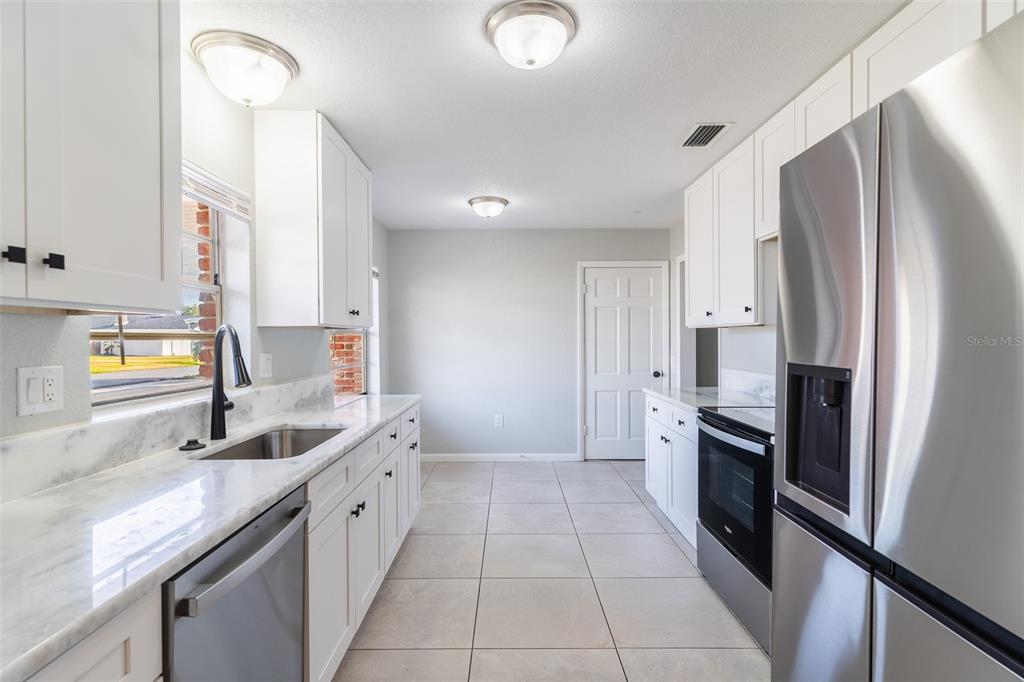 A kitchen features white cabinets, marble-look countertops, stainless steel appliances, and light-colored tile flooring — 124 SHELLEY DRIVE, WINTER HAVEN, FL