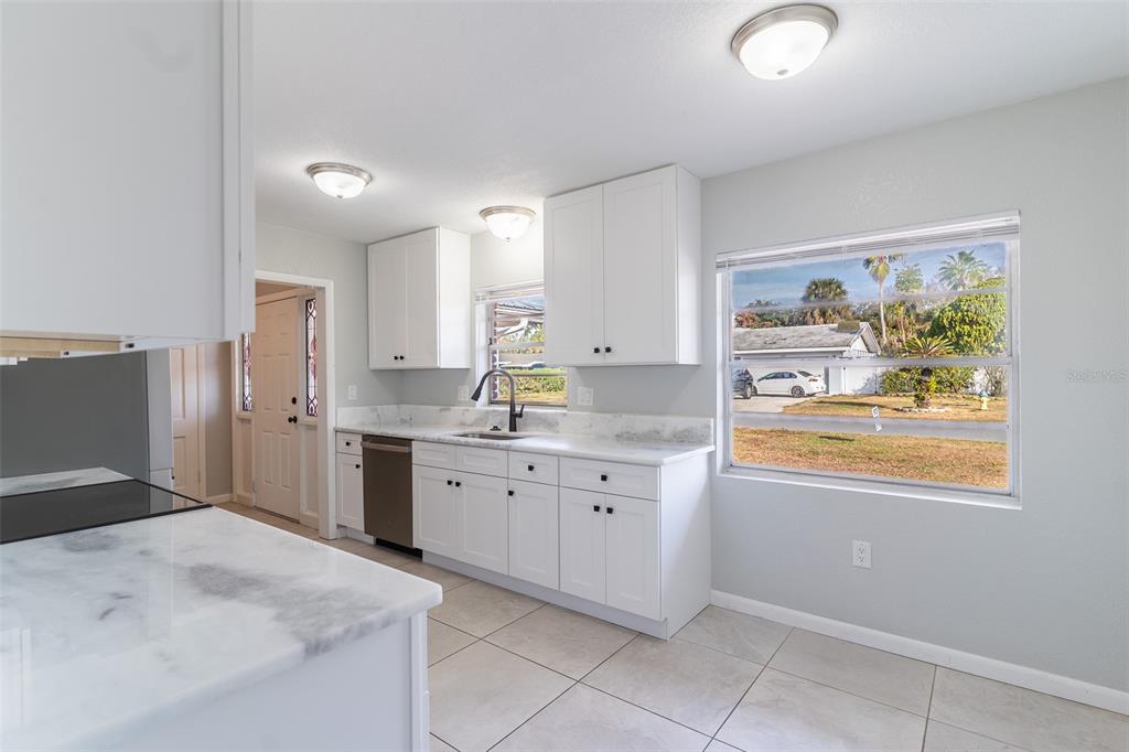A kitchen features white cabinets, marble-look countertops, stainless steel appliances, and tile flooring — 124 SHELLEY DRIVE, WINTER HAVEN, FL