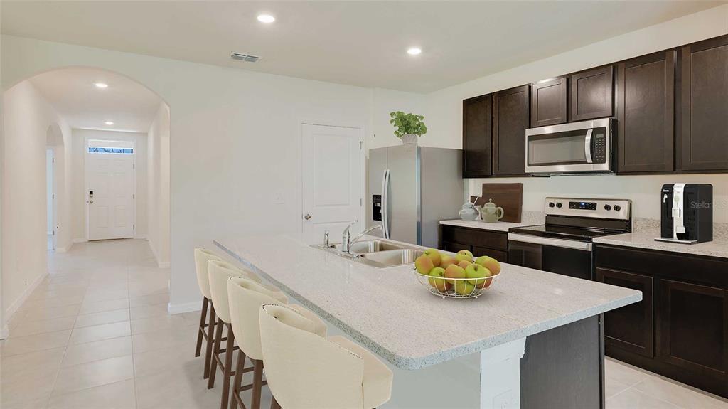 A kitchen features dark wood cabinets, a granite island with bar seating, and stainless appliances — 4644 CONNECTION ROAD, WILDWOOD, FL