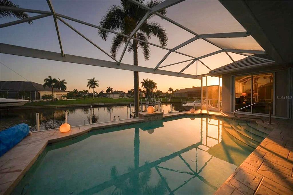 A screened-in swimming pool overlooks a canal at sunset with palm trees in the background — 454 MACEDONIA DRIVE, PUNTA GORDA, FL
