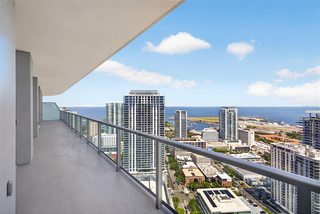 A high-rise balcony with a glass railing overlooks a city skyline and the ocean — 400 CENTRAL AVENUE UNIT 3706, ST PETERSBURG, FL