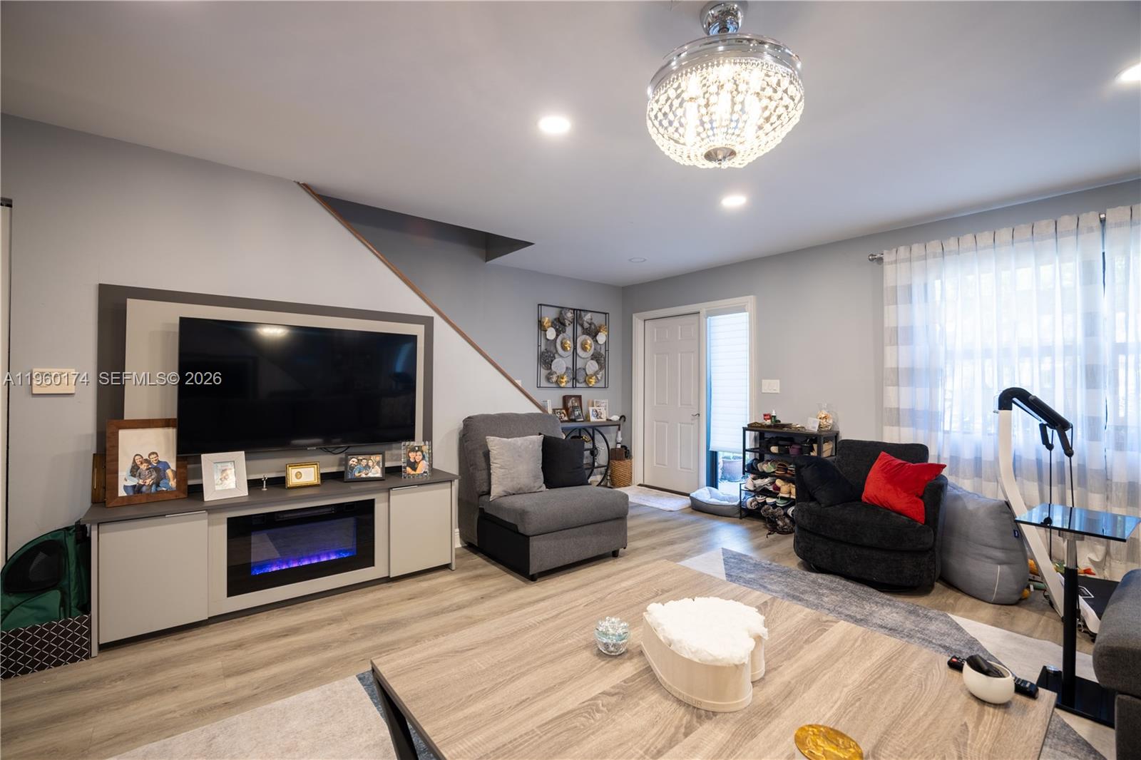 A living room features a television, fireplace console, gray flooring, and a crystal chandelier — 898 NW 47th St, Deerfield Beach FL 33064, DEERFIELD BEACH, FL
