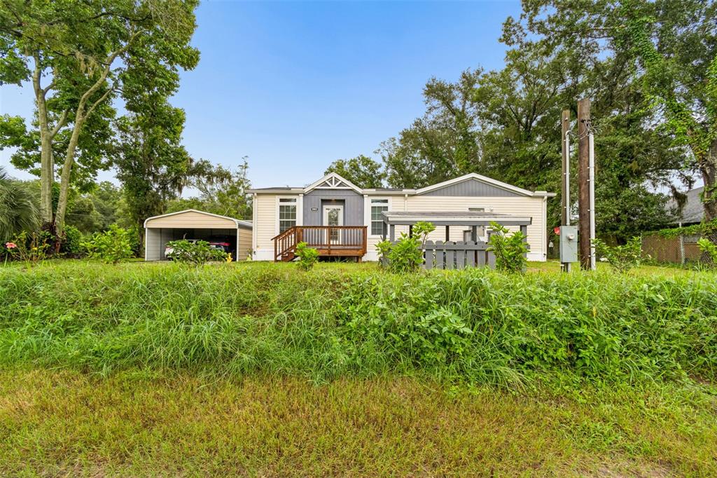 A single-story manufactured home with a carport, wooden deck, and a fenced yard — 9003 SCOTT WILSON LANE, ODESSA, FL