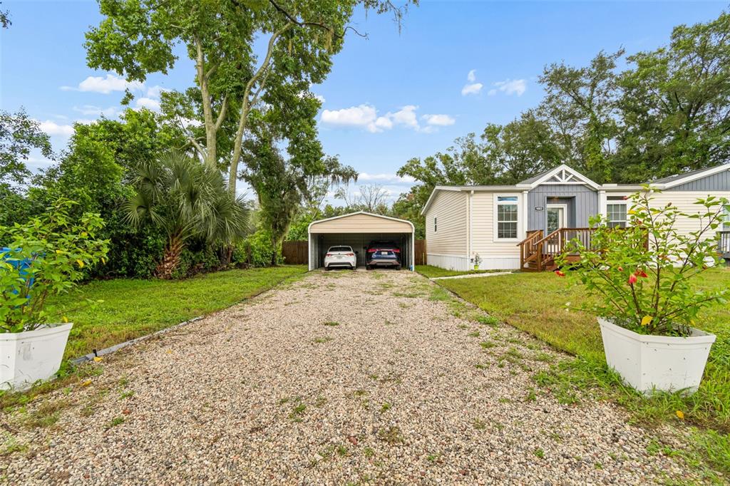 A gravel driveway leads to a metal carport and a single-story house with light siding — 9003 SCOTT WILSON LANE, ODESSA, FL