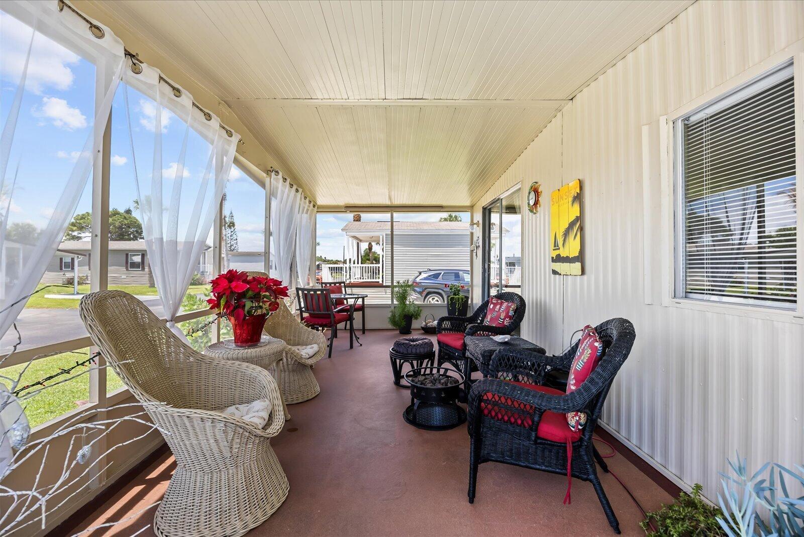 A screened-in porch features wicker furniture, red cushions, and views of a neighboring mobile home — 65 Manor Drive, Fort Pierce FL 34982, FORT PIERCE, FL
