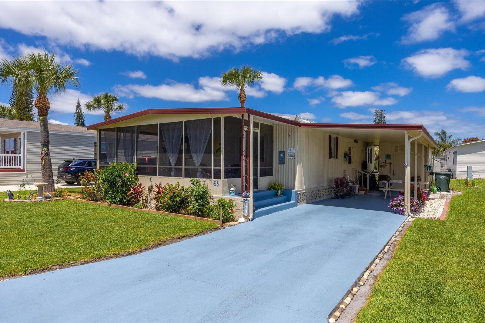 A single-story mobile home with a screened-in porch, blue driveway, and attached carport — 65 Manor Drive, Fort Pierce FL 34982, FORT PIERCE, FL