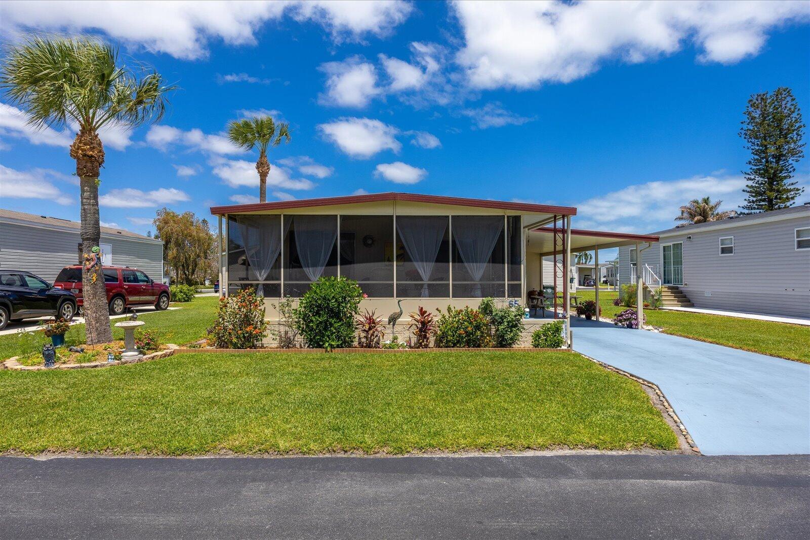 A single-story mobile home with a screened-in front porch, a carport, and a palm tree — 65 Manor Drive, Fort Pierce FL 34982, FORT PIERCE, FL