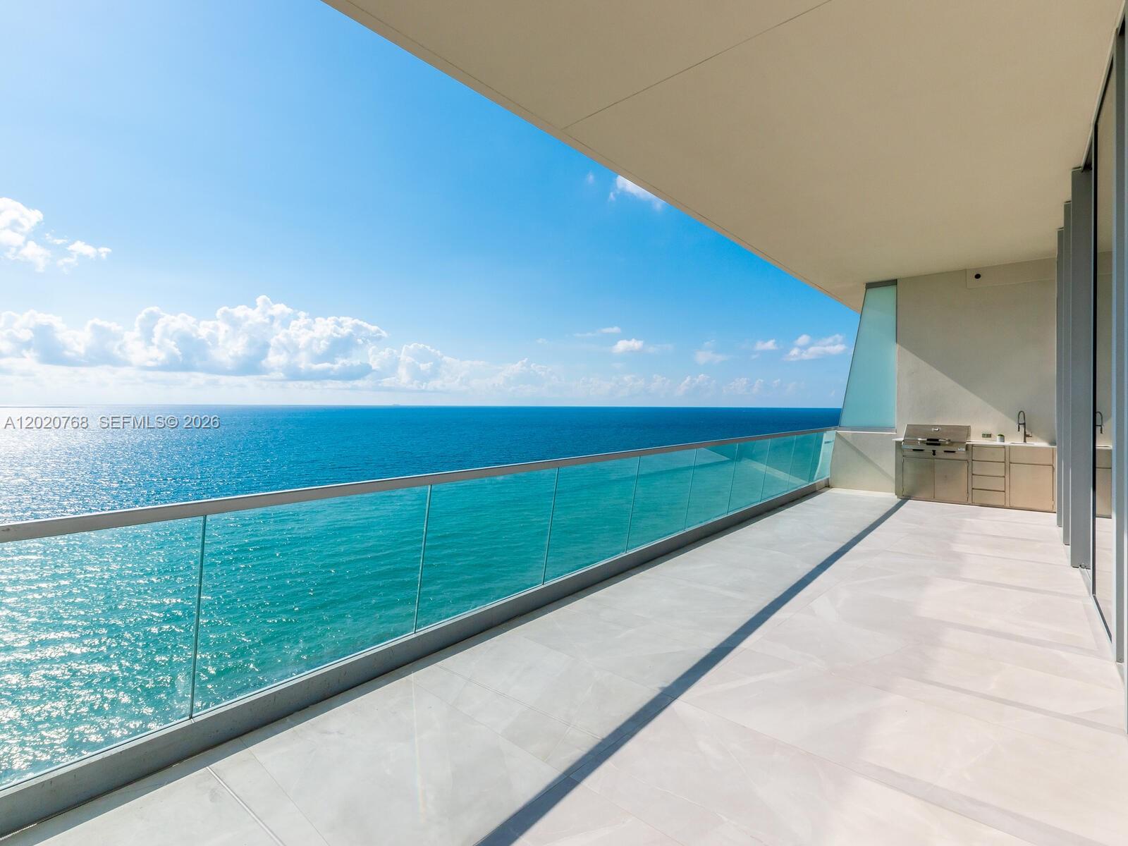 A spacious balcony features a glass railing, light tile flooring, and an outdoor kitchen area — 18501 E Collins # 1503, Sunny Isles Beach FL 33160, SUNNY ISLES BEACH, FL