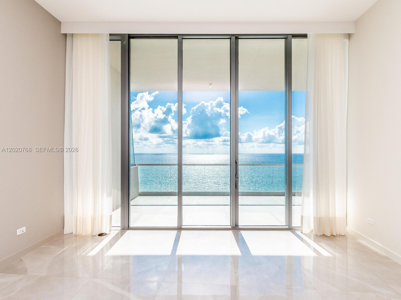 A bright room features floor-to-ceiling glass doors opening to a balcony overlooking the ocean — 18501 E Collins # 1503, Sunny Isles Beach FL 33160, SUNNY ISLES BEACH, FL