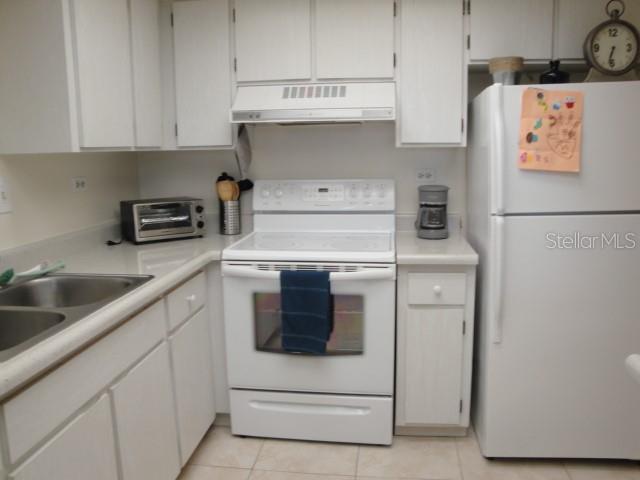 A kitchen features white cabinets, white appliances, a double sink, and light-colored tile flooring — 500 TREASURE ISLAND CAUSEWAY UNIT 202, TREASURE ISLAND, FL