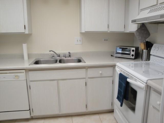 A kitchen featuring white cabinets, a double-basin sink, a dishwasher, and a white electric stove — 500 TREASURE ISLAND CAUSEWAY UNIT 202, TREASURE ISLAND, FL