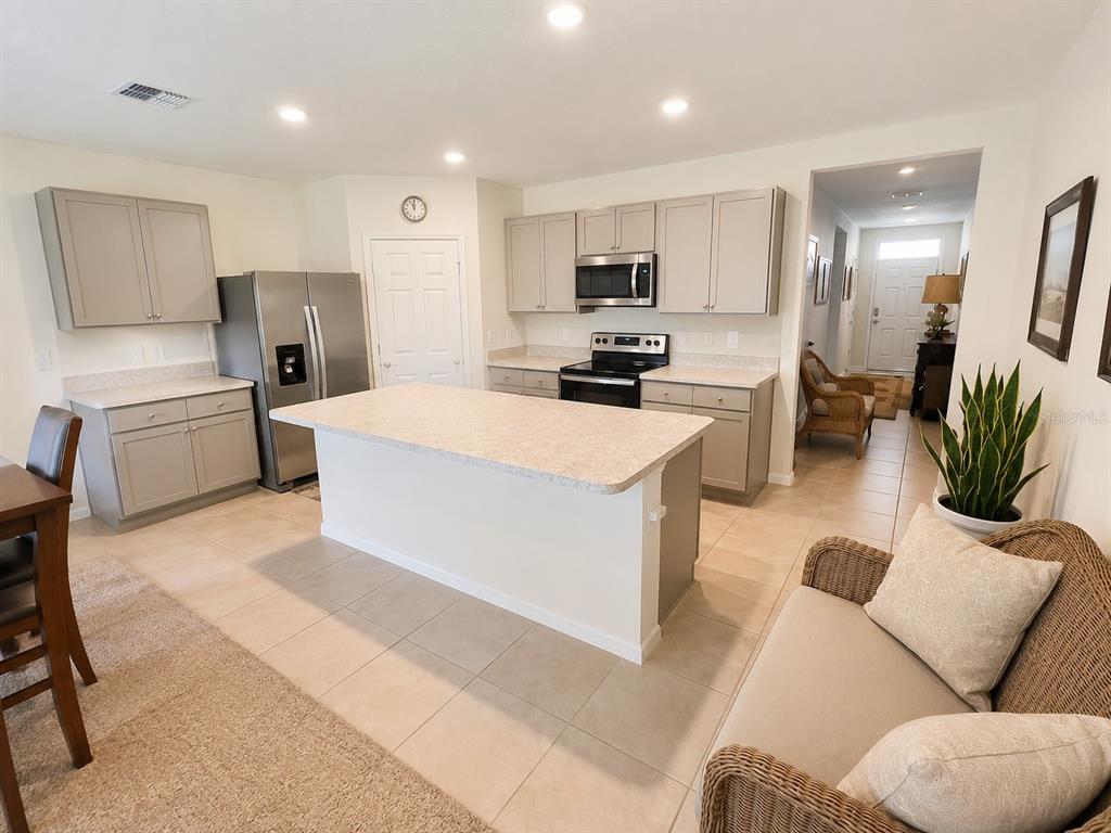 A kitchen features light gray cabinets, stainless steel appliances, a central island, and tile flooring — 2711 NEVERLAND DRIVE, NEW SMYRNA BEACH, FL