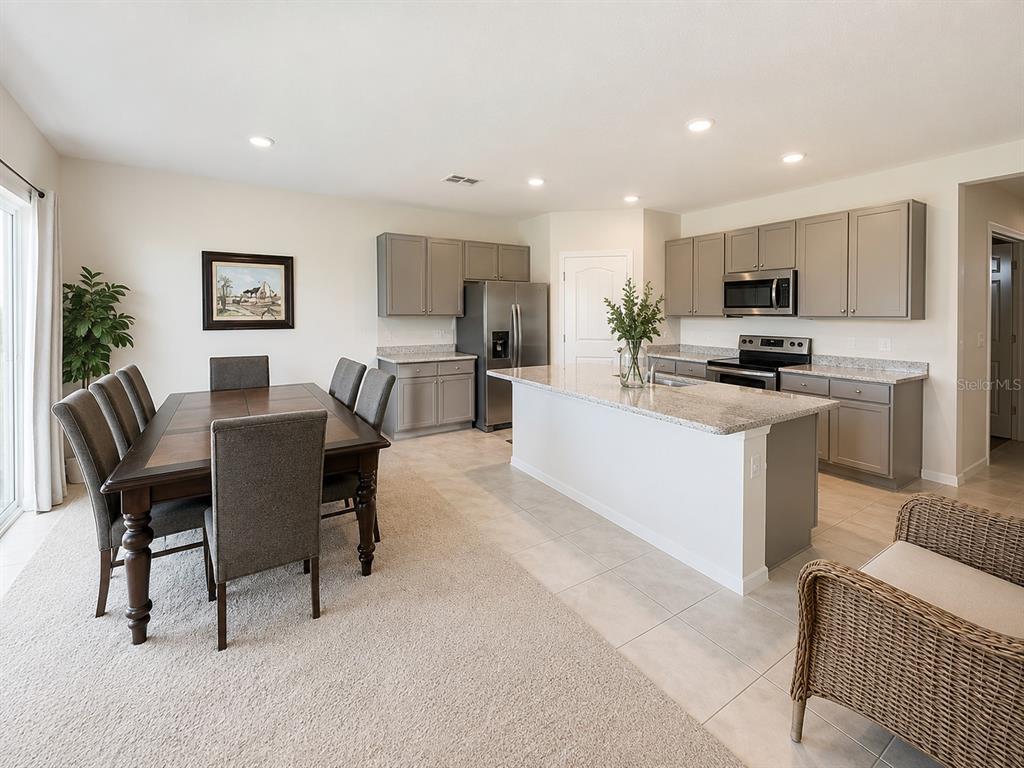 A kitchen with gray cabinets and a granite island flows into a carpeted dining area — 2711 NEVERLAND DRIVE, NEW SMYRNA BEACH, FL