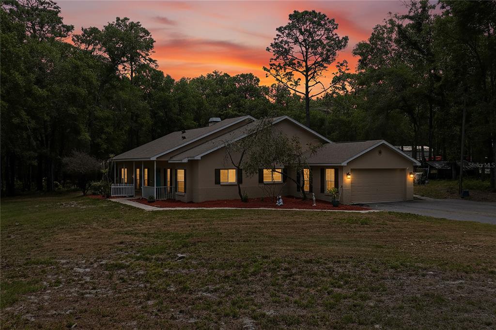 A single-story house with a tan exterior, attached garage, and a porch at sunset — 16225 BONZAI TRAIL, BROOKSVILLE, FL