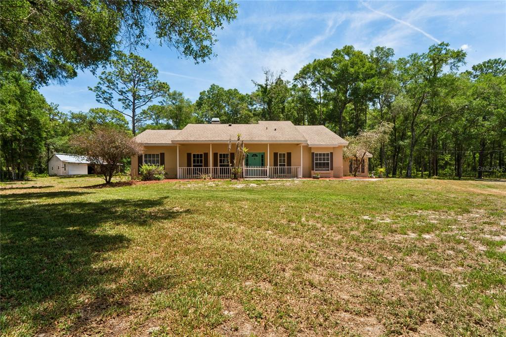 A single-story house with a covered front porch sits on a large, grassy lot — 16225 BONZAI TRAIL, BROOKSVILLE, FL