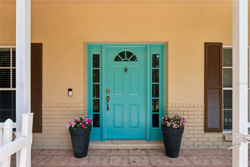 A teal front door with sidelights and two potted flower arrangements sits on a porch — 16225 BONZAI TRAIL, BROOKSVILLE, FL