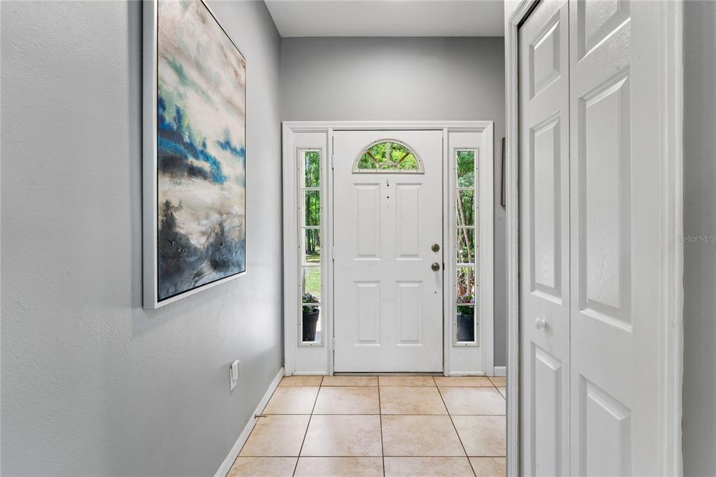An entryway features light tile flooring, gray walls, a white front door, and a wall painting — 16225 BONZAI TRAIL, BROOKSVILLE, FL