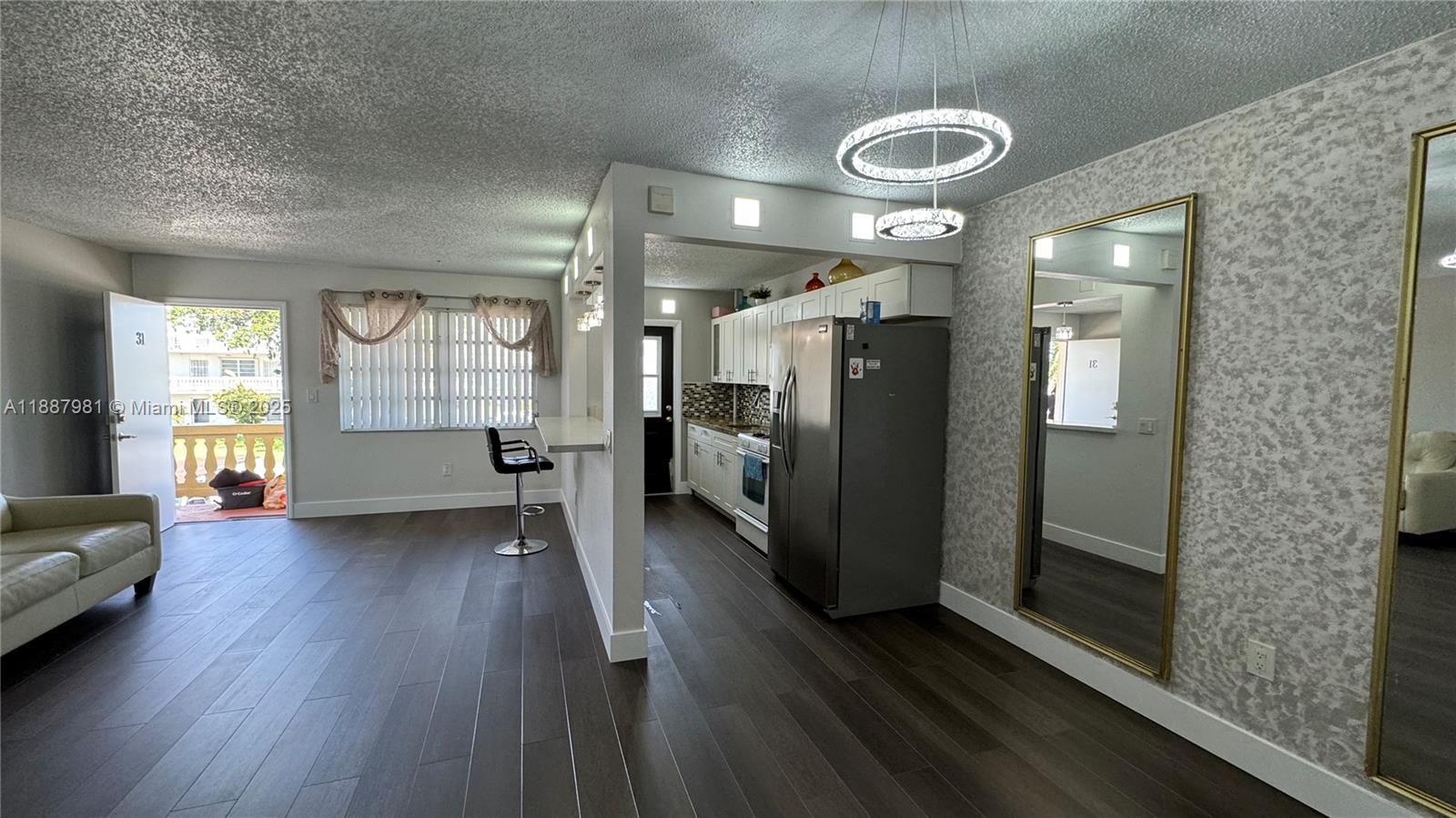 A living room with dark wood floors, a kitchen pass-through, and a large wall mirror — 160 NE 203rd Ter # E31, Miami Gardens FL 33179, MIAMI GARDENS, FL