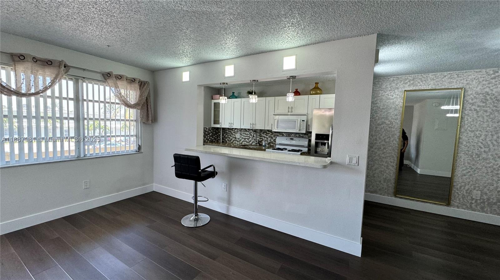 A kitchen with white cabinets and a breakfast bar opens into a living area — 160 NE 203rd Ter # E31, Miami Gardens FL 33179, MIAMI GARDENS, FL