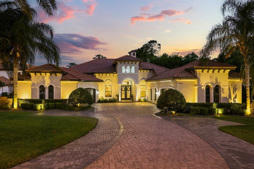 A large, single-story Mediterranean-style house with a paved driveway and palm trees at sunset — 10633 LAGO BELLA DRIVE, ORLANDO, FL