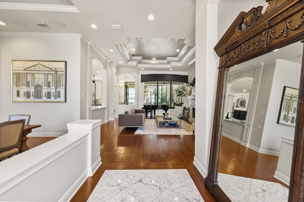 A foyer with marble flooring leads into a living room featuring hardwood floors and coffered ceilings — 10633 LAGO BELLA DRIVE, ORLANDO, FL