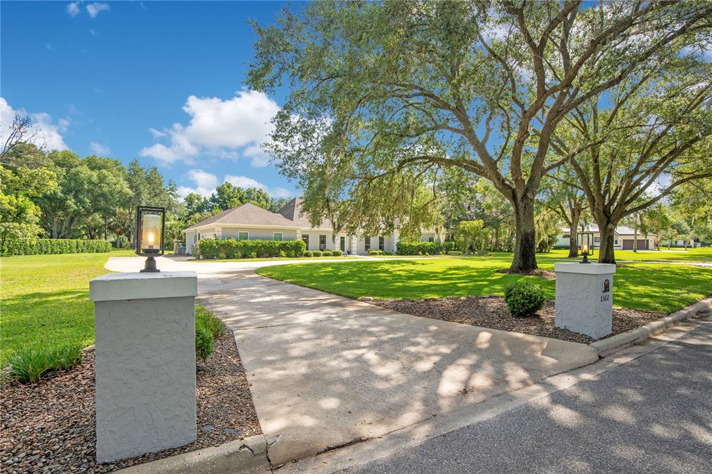 A concrete driveway leads to a single-story house framed by large oak trees — 8368 RAMBLING RIVER DRIVE, SANFORD, FL