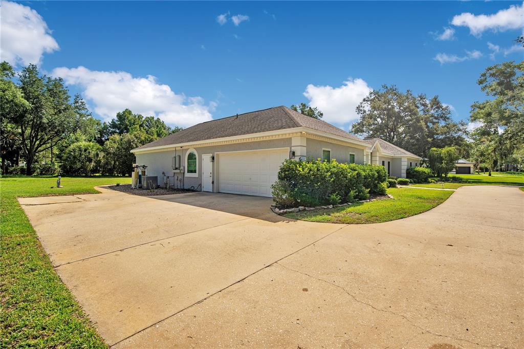 A concrete driveway leads to the side-entry garage of a single-story house with landscaping — 8368 RAMBLING RIVER DRIVE, SANFORD, FL