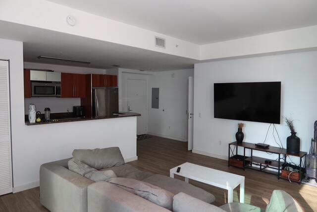 A living room with a gray sectional sofa, a wall-mounted television, and an open kitchen — 300 S Biscayne Boulevard # T1902, Miami FL 33131, MIAMI, FL