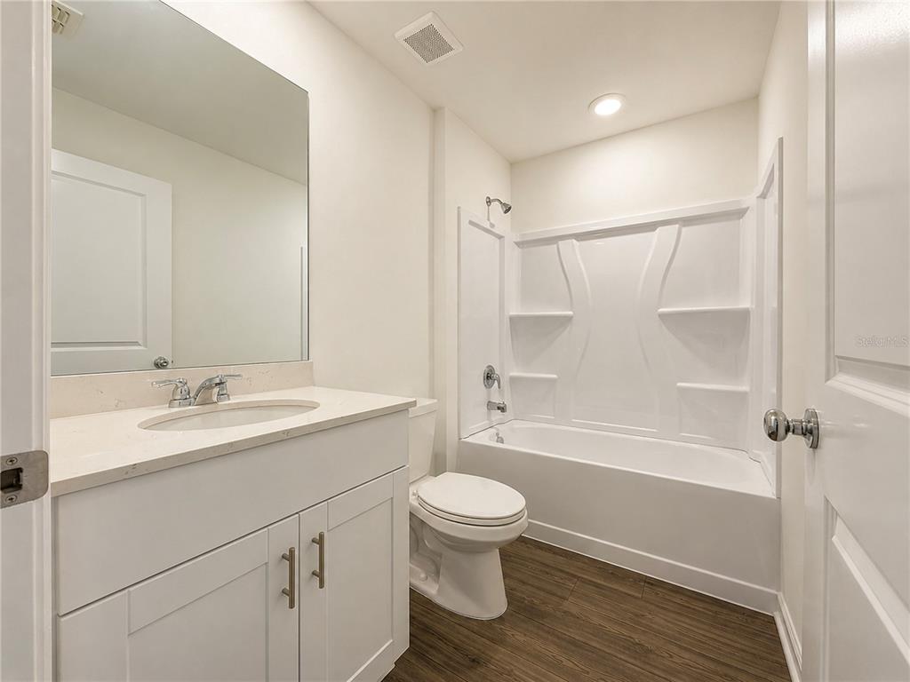 A bathroom features a white vanity, a toilet, and a tub-shower combo with wood-look flooring — 8445 SW 41ST CIRCLE, OCALA, FL