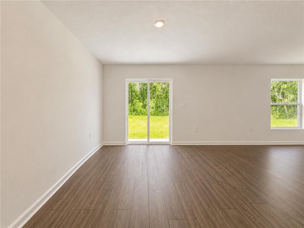 An empty room with wood-look flooring, a sliding glass door, and a single window — 8445 SW 41ST CIRCLE, OCALA, FL