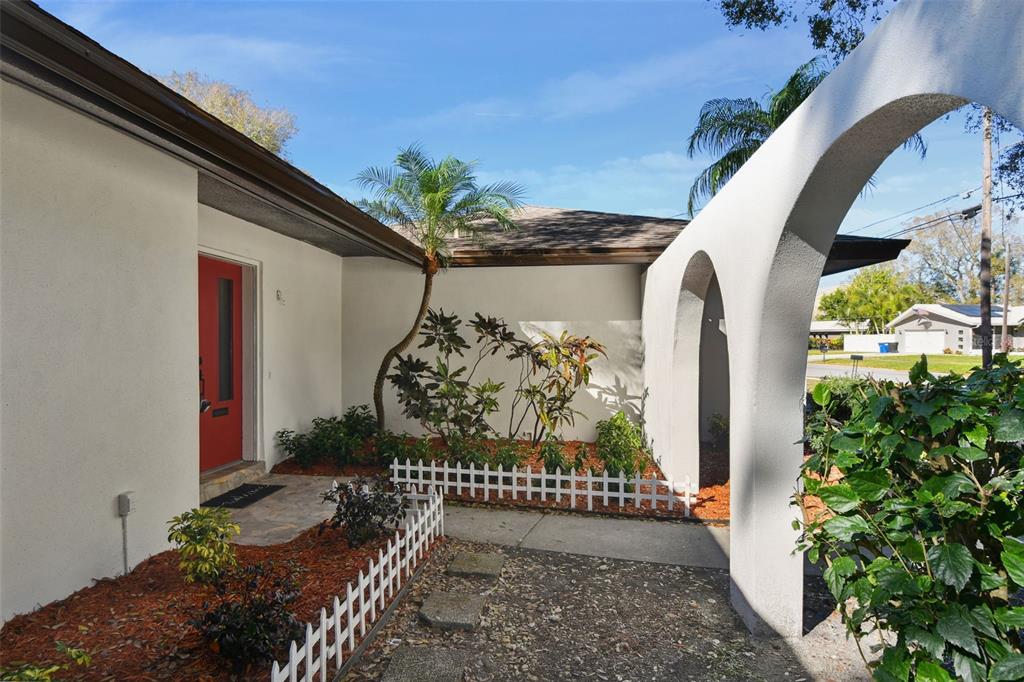 An exterior view of a home entrance with a red door and arched walkway — 570 CASLER AVENUE, CLEARWATER, FL