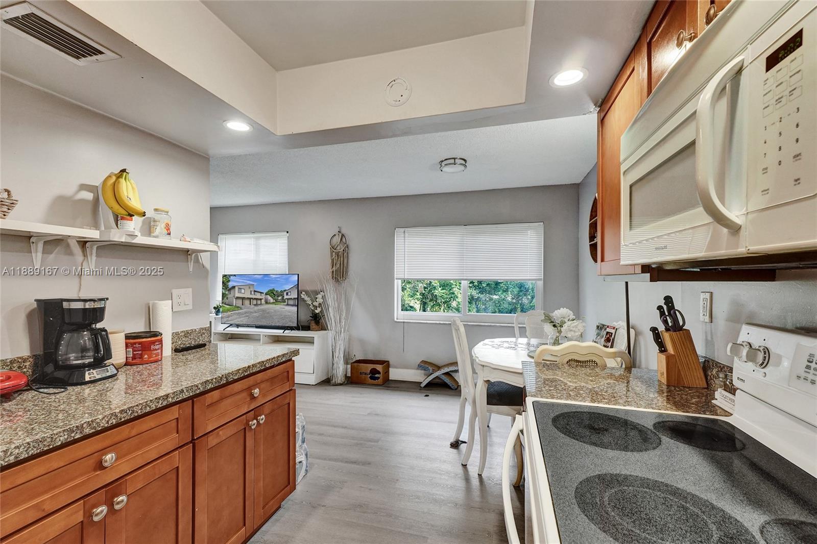 A kitchen with wood cabinets and granite countertops opens into a dining and living area — 2218 NW 59th Way # B, Lauderhill FL 33313, LAUDERHILL, FL