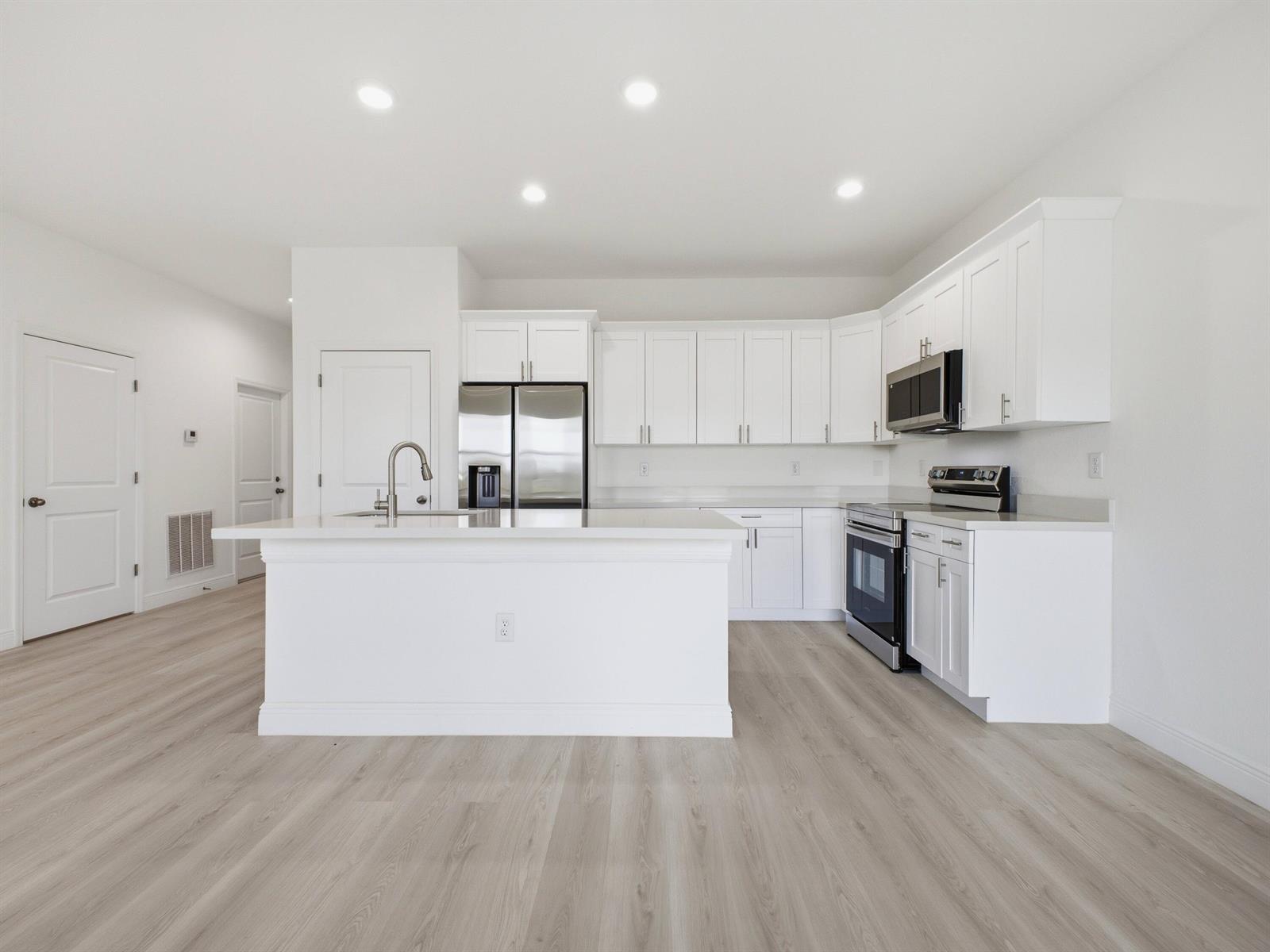 A modern kitchen features white cabinets, stainless steel appliances, and a central island — 3031 NE Beechwood Circle, FL 33935, FL