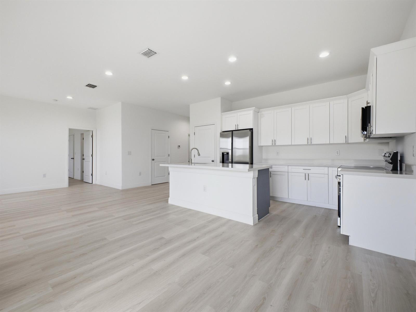 A modern kitchen with white cabinets, a central island, and light wood-look flooring — 3031 NE Beechwood Circle, FL 33935, FL
