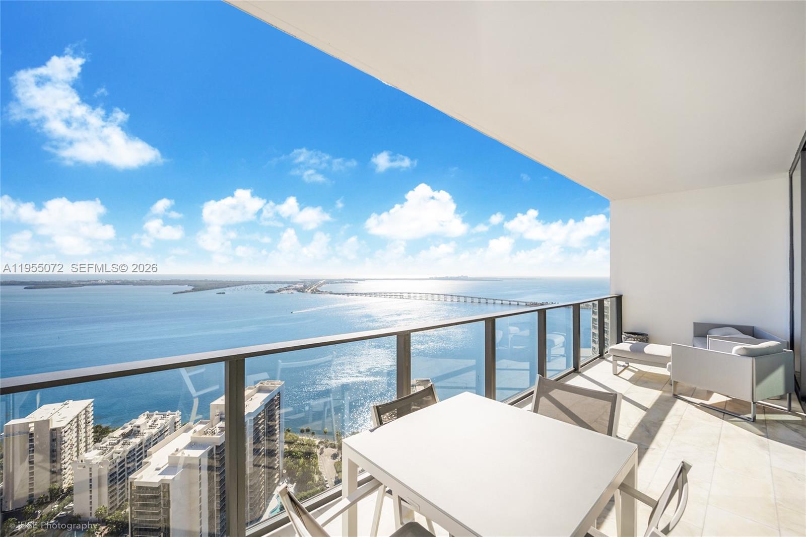 A high-rise balcony features outdoor furniture overlooking a bay and a distant bridge — 1451 Brickell Ave # 3902, Miami FL 33131, MIAMI, FL