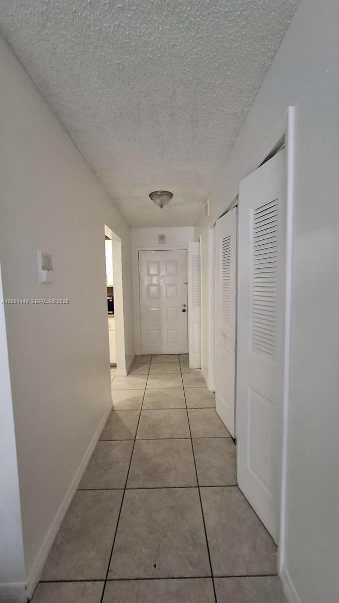 A hallway with light-colored tile flooring leads to a white front door — 6950 Miami Gardens Dr # 201, Hialeah FL 33015, HIALEAH, FL