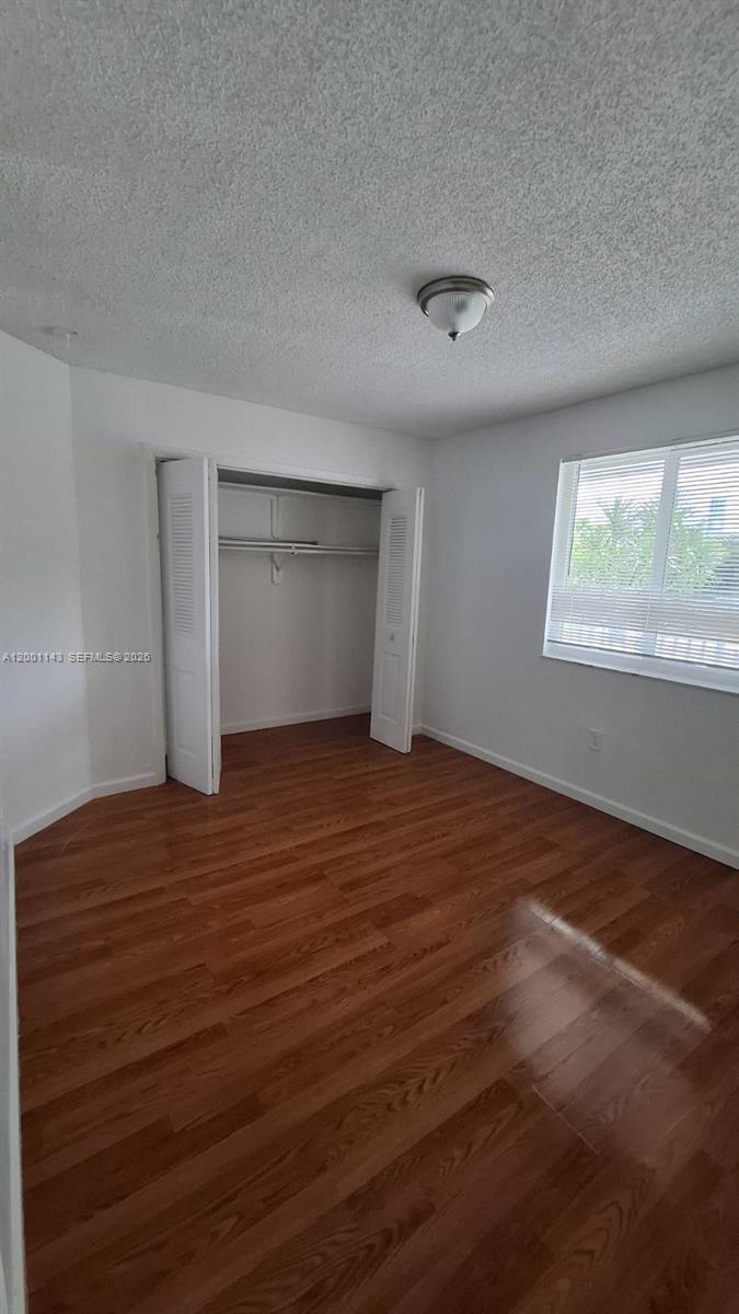 An empty bedroom features white walls, wood-look flooring, a closet with bifold doors, and a window — 6950 Miami Gardens Dr # 201, Hialeah FL 33015, HIALEAH, FL