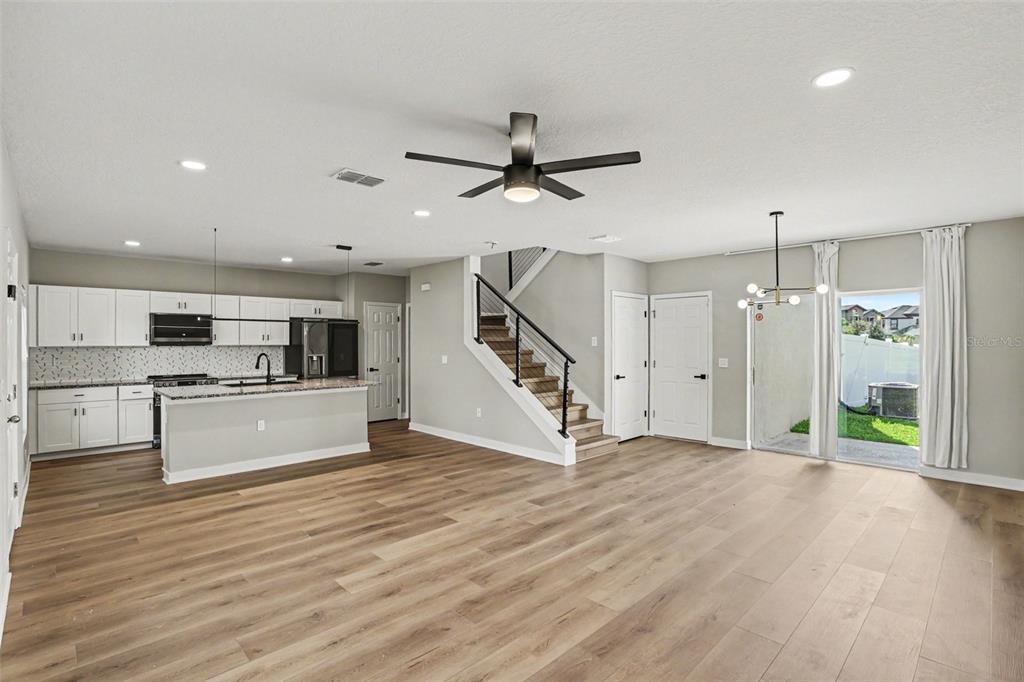 An open-concept kitchen and living area features white cabinetry, wood-look flooring, and a staircase — 12531 TRIPLE CREEK BOULEVARD, RIVERVIEW, FL