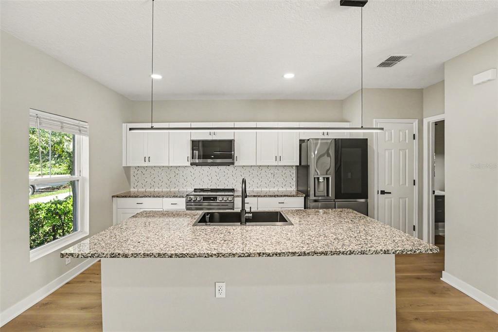 A modern kitchen features white cabinets, granite countertops, a large island, and stainless steel appliances — 12531 TRIPLE CREEK BOULEVARD, RIVERVIEW, FL
