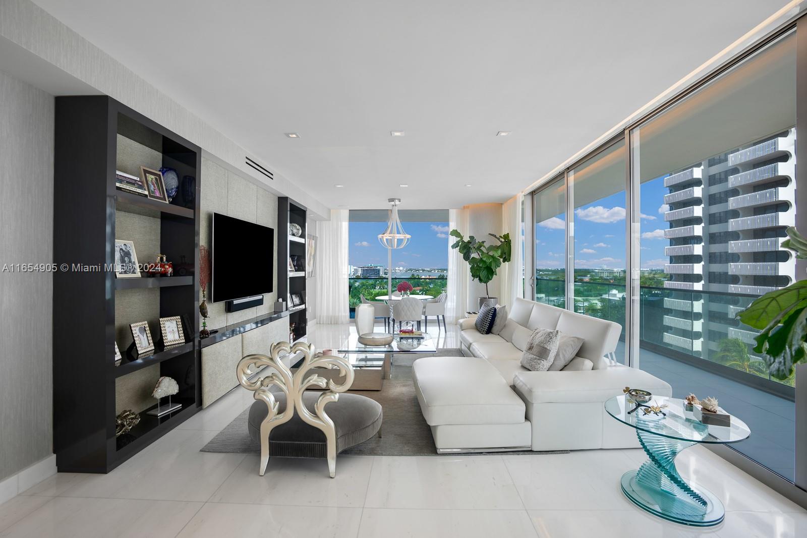 A modern living room features a white sectional sofa, a black shelving unit, and floor-to-ceiling windows — 10203 Collins Ave # 801, Bal Harbour FL 33154, BAL HARBOUR, FL