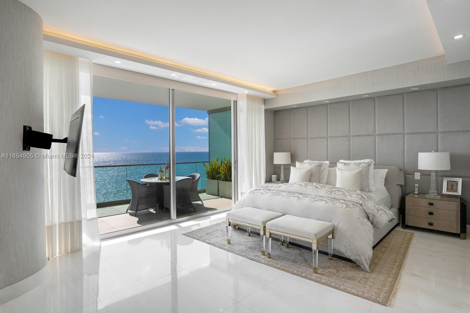 A modern bedroom features a large bed, gray tufted headboard, and a balcony overlooking the ocean — 10203 Collins Ave # 801, Bal Harbour FL 33154, BAL HARBOUR, FL