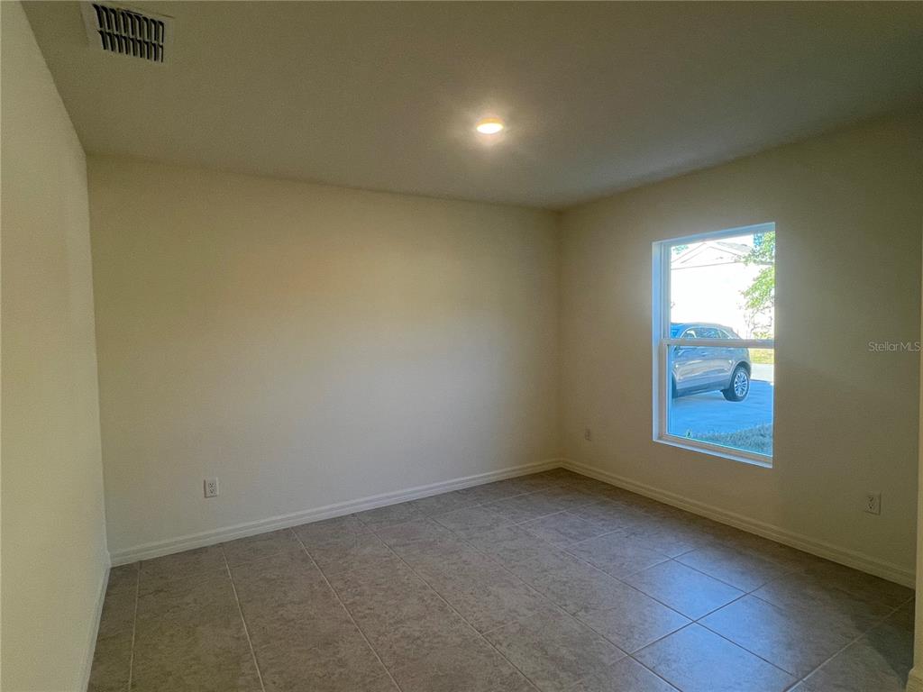An empty room features beige walls, light-colored tile flooring, a single window, and a ceiling vent — 87 BRESSLER LANE, PALM COAST, FL