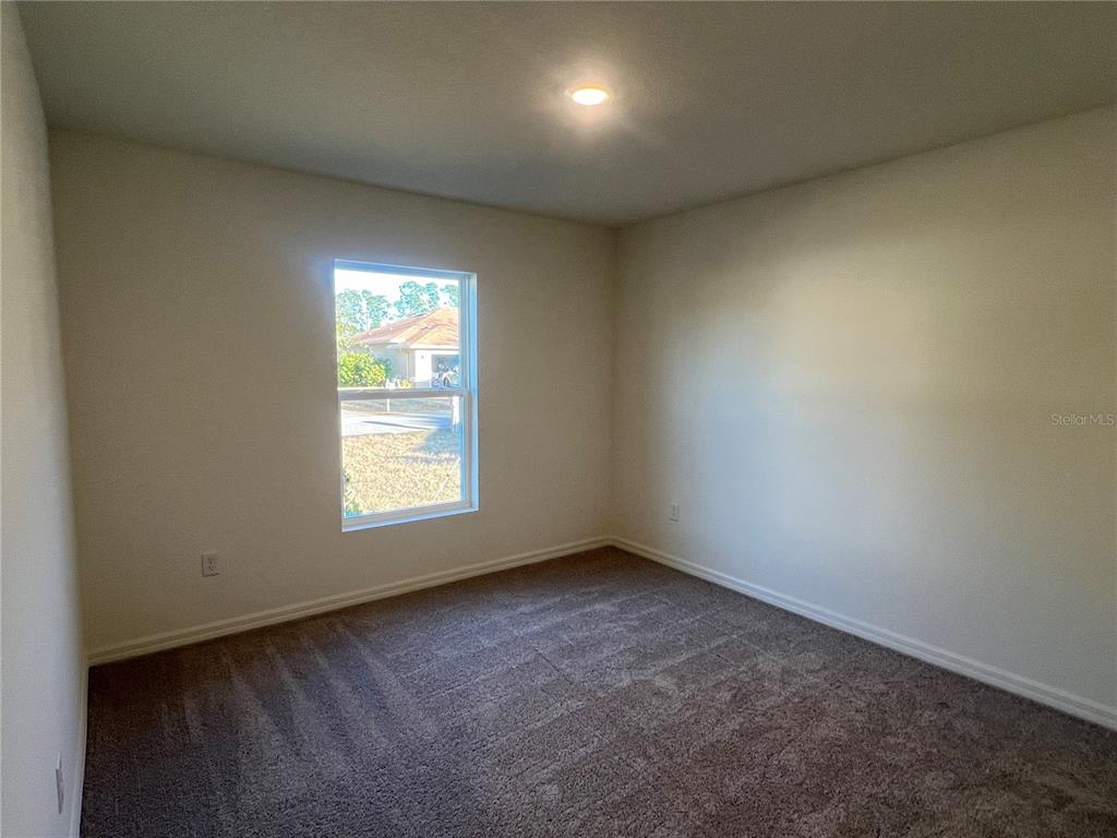 An empty bedroom features beige walls, brown carpeting, and a single window — 87 BRESSLER LANE, PALM COAST, FL