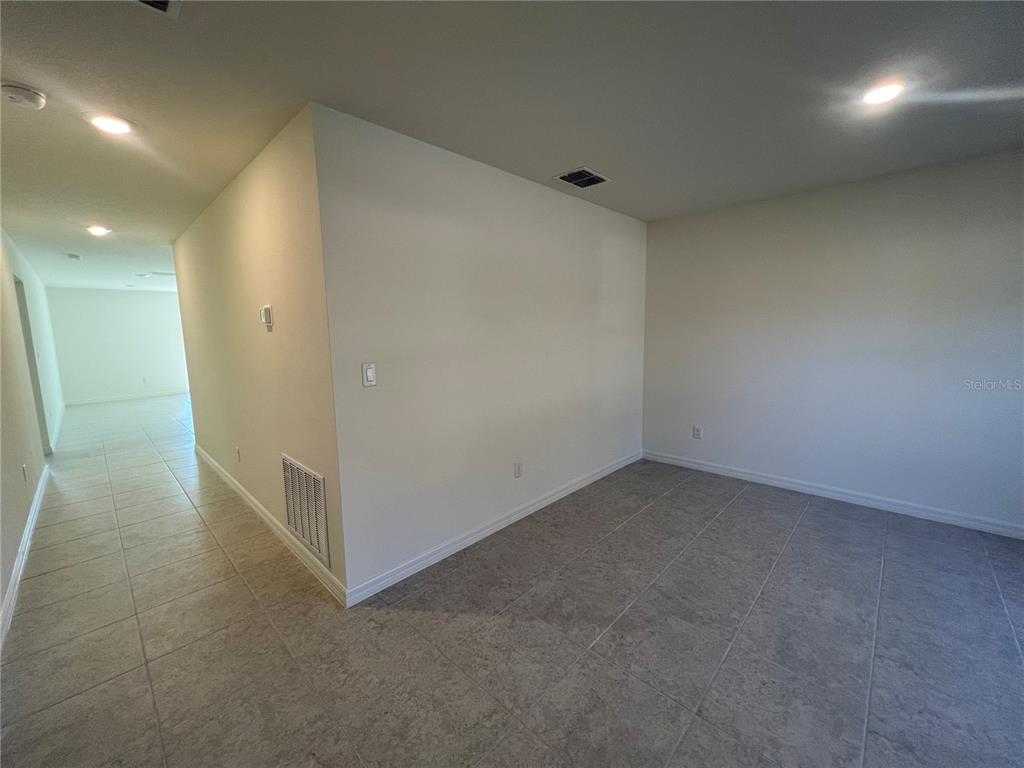 An empty room with light-colored tile flooring and white walls leads to a long hallway — 87 BRESSLER LANE, PALM COAST, FL