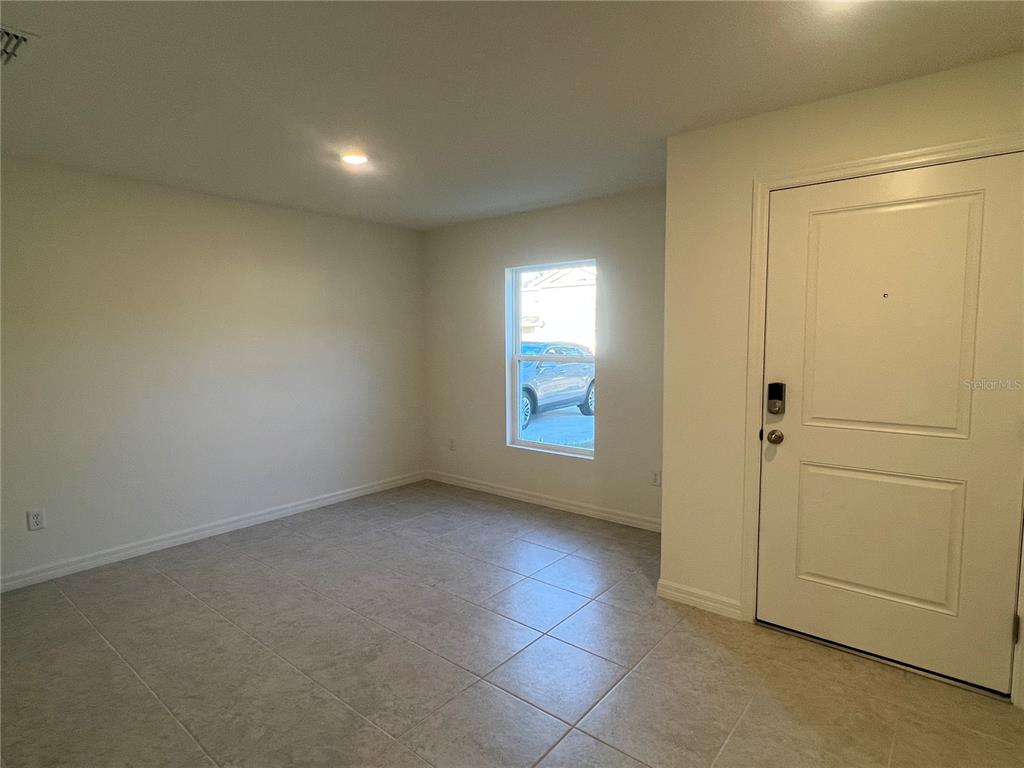 An empty room with light-colored tile flooring, a single window, and a white front door — 87 BRESSLER LANE, PALM COAST, FL