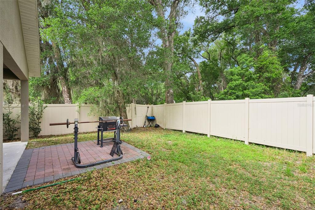 A backyard features a brick patio with a weight rack and grill against a vinyl fence — 520 S KENTUCKY AVENUE, DELAND, FL