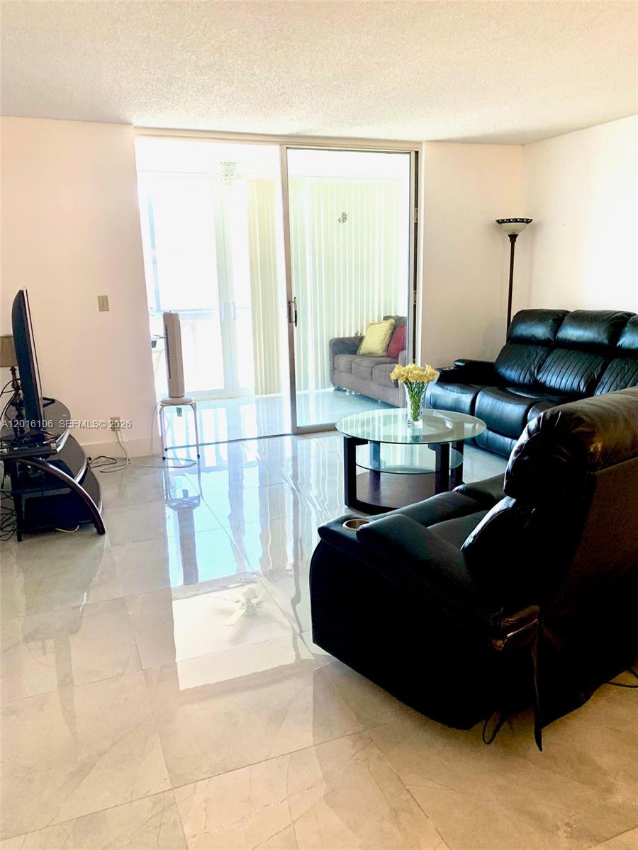A living room features black leather furniture, a glass coffee table, and tile flooring — 501 NE 14th Ave # 601, Hallandale Beach FL 33009, HALLANDALE BEACH, FL