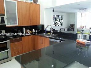A kitchen features wood cabinets, black countertops, and a stainless steel oven — 546 NE 199th Ln # 4W, Miami FL 33179, MIAMI, FL